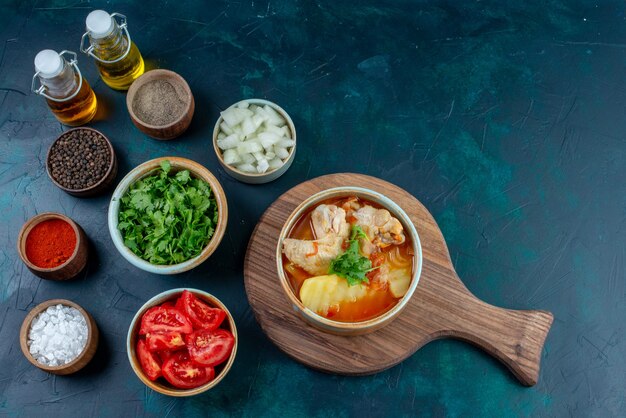 Vue de dessus soupe au poulet avec pommes de terre avec sel, poivre, légumes frais et huile sur le bureau bleu foncé soupe viande repas dîner