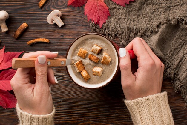 Vue de dessus de la soupe aux champignons d'hiver dans la tasse avec les mains tenant la cuillère