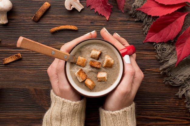 Photo gratuite vue de dessus de la soupe aux champignons d'hiver dans une tasse tenue à la main avec des croûtons et une cuillère