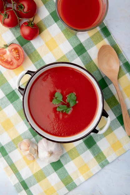 Photo gratuite vue de dessus de la soupe aux tomates avec une cuillère et des légumes sur une surface en tissu écossais