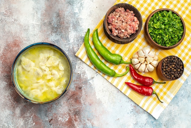 Vue de dessus de la soupe de boulettes de dushbara dans un bol de piments forts à l'ail cuillère en bois bols avec des verts de viande et du poivre noir sur un torchon sur une surface nue