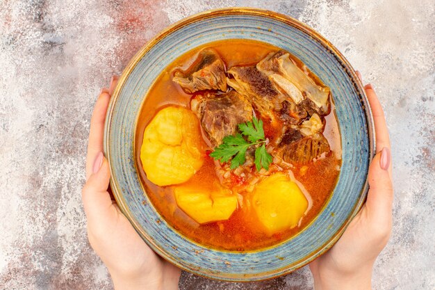 Vue de dessus de la soupe bozbash dans un bol dans une main féminine sur fond nu