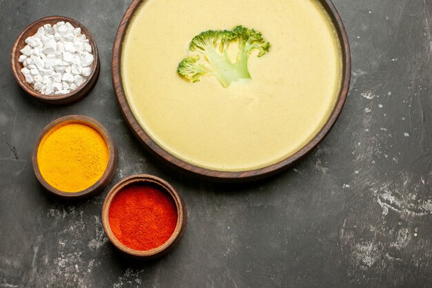 Vue de dessus de la soupe de brocoli crémeuse dans un bol brun et différentes épices sur tableau gris