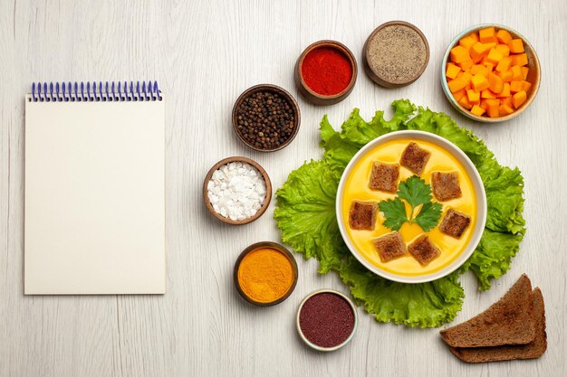 Vue de dessus de la soupe à la citrouille avec de petites biscottes et assaisonnements sur blanc