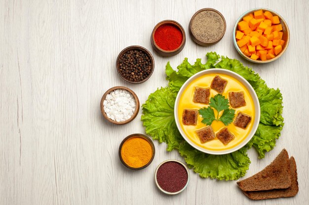 Vue de dessus de la soupe à la citrouille avec de petites biscottes et assaisonnements sur blanc