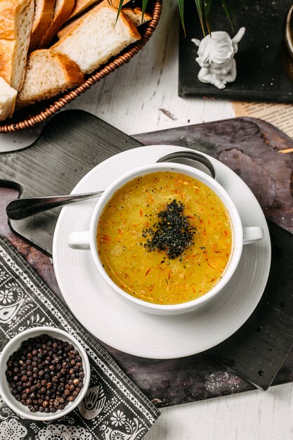 Vue de dessus de la soupe de pois et lentilles au safran et aux herbes dans un bol blanc