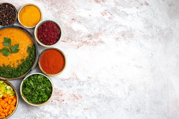 Vue de dessus une soupe savoureuse avec des légumes verts et différents assaisonnements sur un bureau blanc