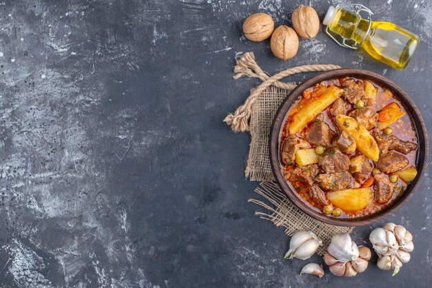 Vue de dessus de la soupe de viande bozbash dans un bol en bois bouteille d'huile de noix d'ail sur une table grise avec espace libre