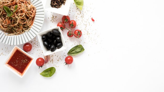 Vue de dessus des spaghettis aux olives; tomate; feuille de basilic; herbes sur fond blanc