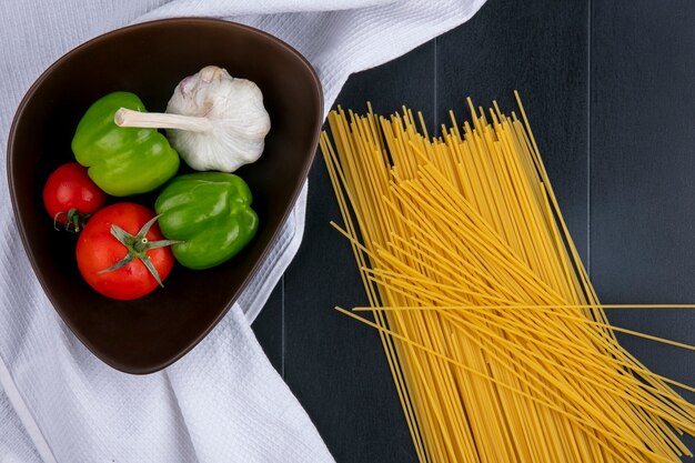 Vue de dessus des spaghettis crus aux tomates ail et poivron dans un bol sur une serviette blanche sur une surface noire