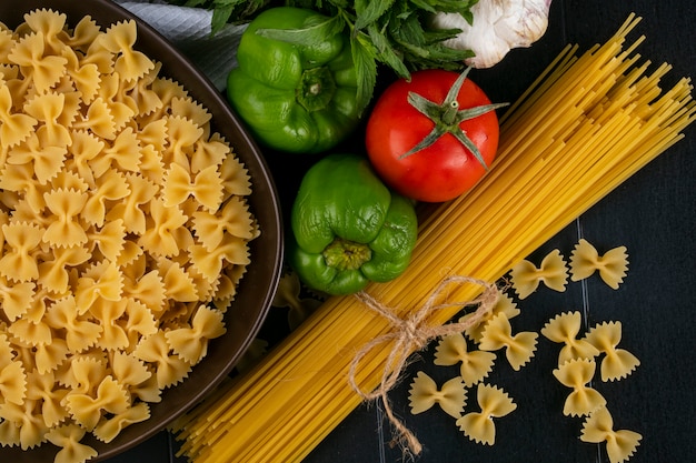 Vue de dessus des spaghettis crus avec des pâtes crues dans un bol avec des tomates ail et poivron sur une surface noire