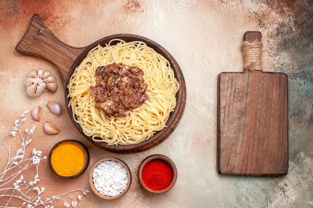 Vue de dessus des spaghettis cuits avec de la viande hachée sur un assaisonnement pour pâtes de bureau en bois