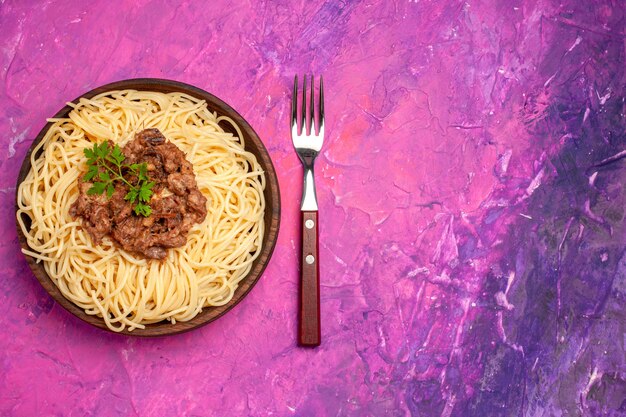 Vue de dessus des spaghettis cuits avec de la viande hachée sur des pâtes de pâte à plat de couleur rose clair