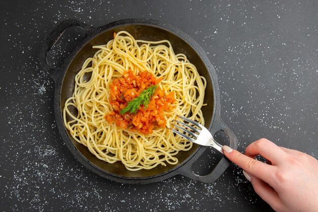 Vue de dessus des spaghettis avec sauce dans une fourchette de poêle à frire dans une main féminine sur un espace libre de table noire