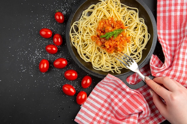 Vue de dessus des spaghettis avec sauce dans une fourchette de poêle à frire dans des tomates cerises à la main sur un espace libre de table noire