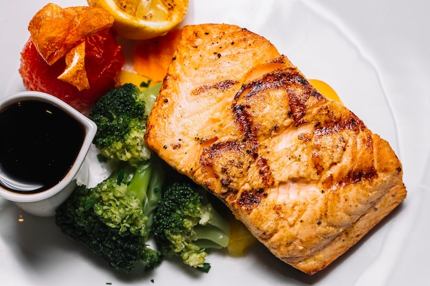 Vue de dessus steak de poisson rouge grillé avec brocoli une tranche de tomate citron et sauce narsharab