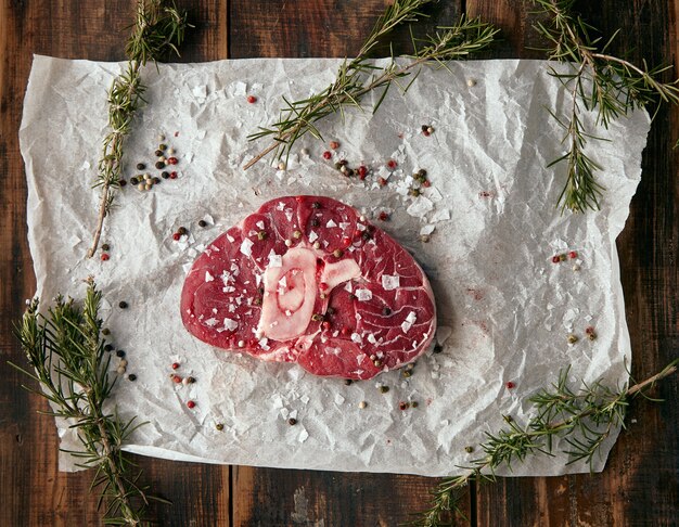 Vue de dessus steak de viande avec os sur papier kraft, salé. poivré et avec romero