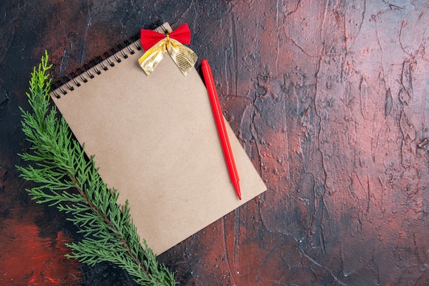 Vue de dessus stylo rouge sur un bloc-notes avec petit arc une branche de pin sur une surface rouge foncé avec espace de copie