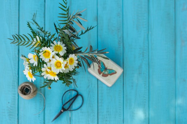 Vue de dessus de la surface en bois avec des marguerites, des ciseaux et boîte