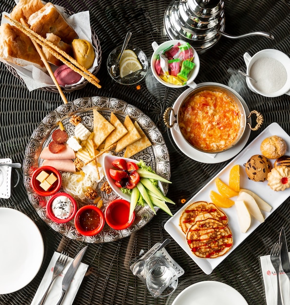 Vue de dessus de la table du petit-déjeuner avec des œufs confitures crêpes saucisses au fromage