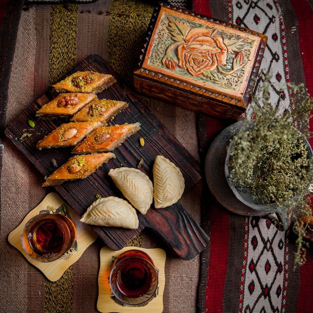 Vue de dessus table sucrée avec baklava et shekerbura et verre de thé en planche à découper