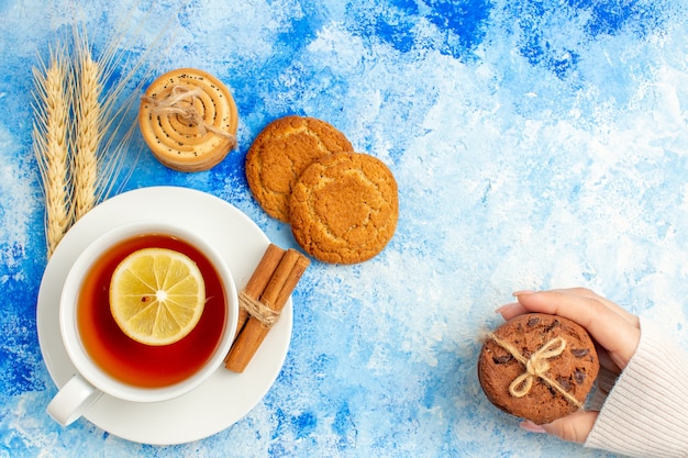 Vue de dessus tasse de biscuits au thé dans la main féminine sur l'espace libre de la table bleue