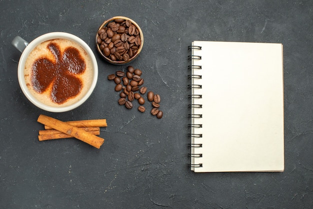 Vue de dessus une tasse de bol de café avec des graines de café bâtons de cannelle un bloc-notes sur fond sombre isolé