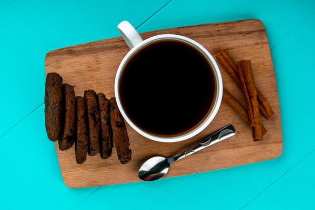 Vue de dessus d'une tasse de café et de biscuits avec une cuillère sur une planche à découper sur fond bleu