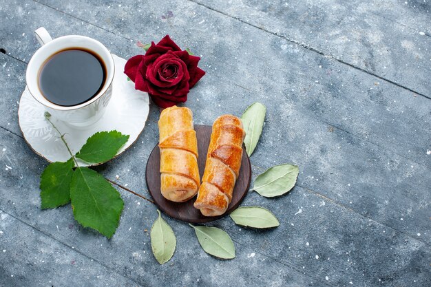 Vue de dessus de la tasse de café avec des bracelets délicieux sucrés et rose rouge sur bois gris, sucre de gâteau pâtisserie sucré