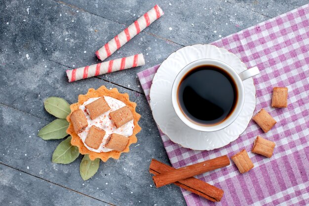 Vue de dessus de la tasse de café chaud et fort avec gâteau et cannelle sur gris, boisson sucrée de bonbons au café