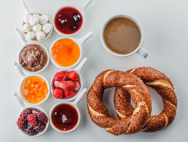 Photo gratuite vue de dessus une tasse de café avec des confitures, framboise, sucre, chocolat dans des tasses et bagel turc sur une surface blanche