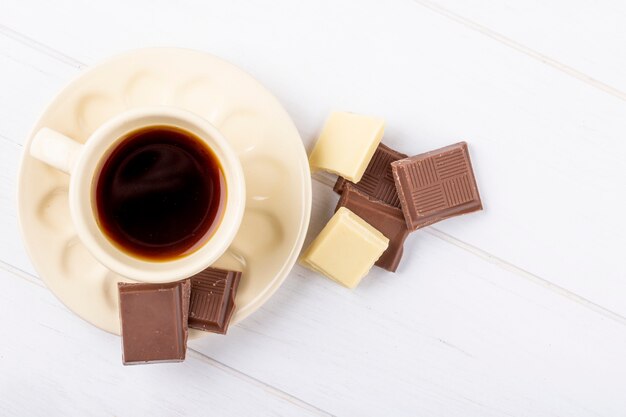 Vue de dessus d'une tasse de café avec du chocolat blanc et noir sur fond de bois blanc