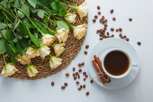 Vue de dessus une tasse de café avec des fleurs sur un dessous de plat sur une surface blanche. horizontal