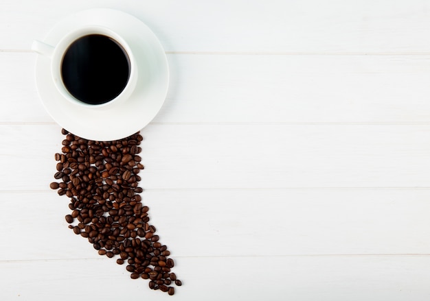 Vue de dessus d'une tasse de café et de grains de café éparpillés sur fond blanc avec copie espace