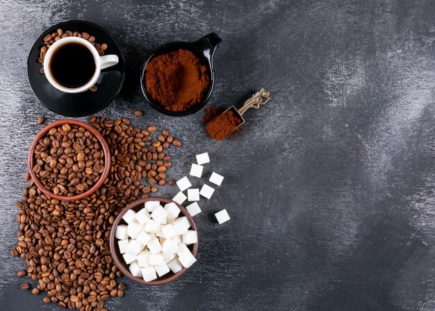 Vue de dessus une tasse de café avec des grains de café et des morceaux de sucre sur une table sombre