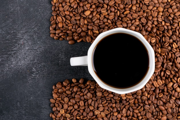 Vue de dessus de tasse de café avec des grains de café sur une table sombre