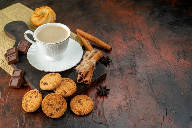 Vue de dessus d'une tasse de café sur une planche à découper en bois cookies barres de chocolat cannelle limes sur le côté droit sur une surface sombre