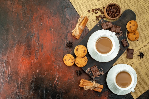 Vue de dessus d'une tasse de café sur une planche à découper en bois sur un vieux biscuits de journaux barres de chocolat cannelle limes sur le côté gauche sur fond sombre