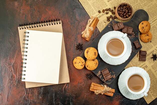 Vue de dessus d'une tasse de café sur une planche à découper en bois sur un vieux journal biscuits cannelle limes barres de chocolat cahier à spirale