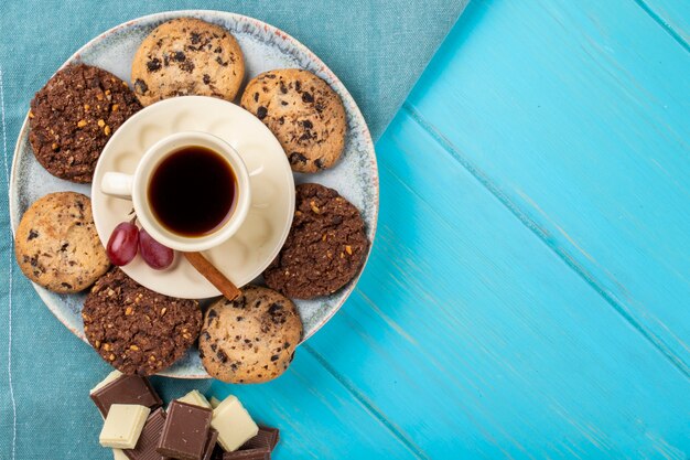 Vue de dessus d'une tasse de café servi avec des biscuits à l'avoine et du chocolat sur fond bleu avec copie espace