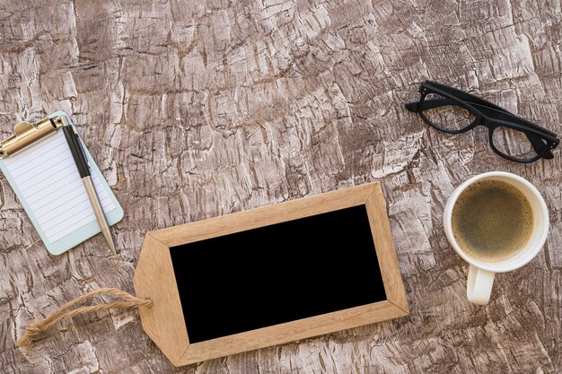 Une vue de dessus d&#39;une tasse de café; stylo; petit presse-papiers et lunettes sur fond texturé