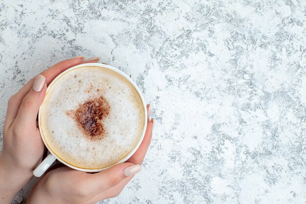 Vue de dessus de la tasse à cappuccino dans une main féminine sur une surface grise avec lieu de copie