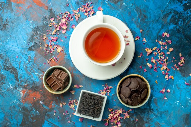 Vue de dessus une tasse de chocolats au thé dans des bols sur une surface bleu rouge