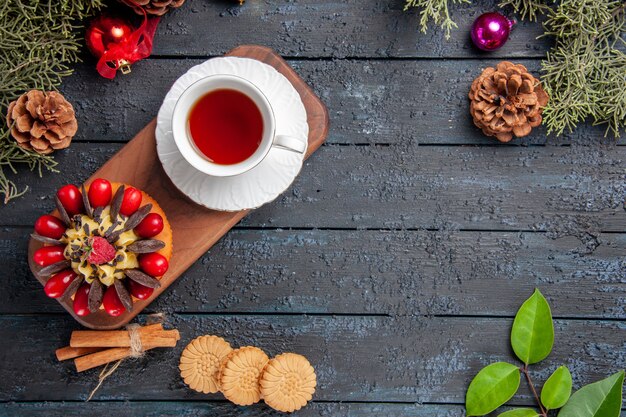 Vue de dessus une tasse de gâteau thé et baies sur une assiette en bois cannelle pommes de pin jouets de Noël biscuits et feuilles sur table en bois foncé