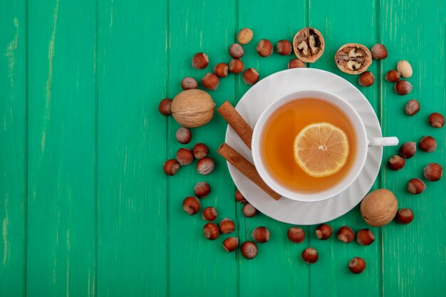 Vue de dessus de la tasse de hot toddy avec du citron à l'intérieur et de la cannelle sur une soucoupe avec motif de noix et de noix autour sur fond vert avec espace copie