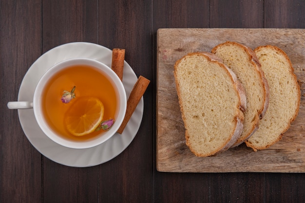 Vue de dessus de la tasse de hot toddy avec fleur de citron à l'intérieur et cannelle sur soucoupe avec du pain croustillant en tranches sur une planche à découper sur fond de bois