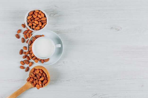 Vue de dessus tasse de lait aux amandes dans des cuillères en bois sur fond de bois blanc. espace libre horizontal pour votre texte