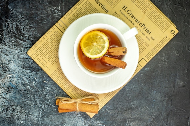Vue de dessus tasse de thé aromatisée au citron et à la cannelle sur des bâtons de cannelle de journal sur une table sombre