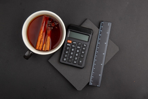Photo gratuite vue de dessus tasse de thé aromatisée par le bloc-notes de la calculatrice à la cannelle sur une table sombre