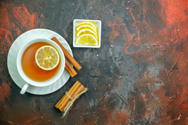 Vue de dessus tasse de thé aromatisée par des tranches de citron citron dans un petit bol de cannelle sur fond rouge foncé